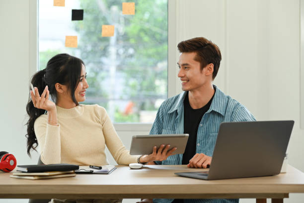 dua rekan kerja yang tersenyum sedang mendiskusikan proyek bekerja sama di kantor kreatif